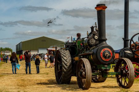 Photo for The Battle of Britain Memorial Flight Lancaster, Spitfire and Hurricane fly over the vintage steam traction engines at the Carrington Steam and Vintage Rally in Carrington in Lincolnshire - Royalty Free Image