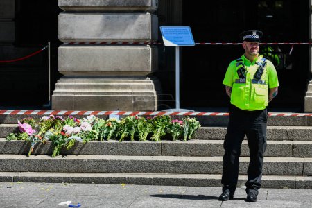 Foto de Ataques de Nottingham: Un policía vigila los homenajes florales dejados en las escaleras del edificio Council House en el centro de la ciudad hoy después de los ataques de ayer que dejaron 3 personas muertas y 3 heridas Nottingham, Reino Unido, 13 de junio de 2023 - Imagen libre de derechos