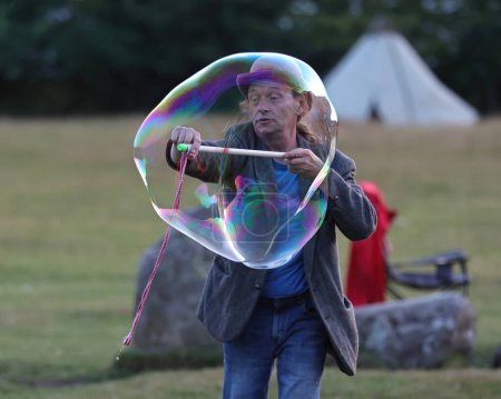Téléchargez les photos : Un participant divertit alors qu'il souffle des bulles géantes lors de la célébration du solstice d'été du Cercle de pierre de Castlerigg, Royaume-Uni, 20 juin 2023 - en image libre de droit