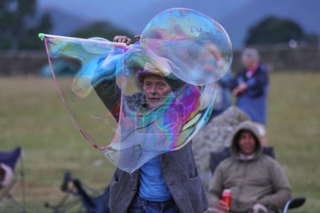 Téléchargez les photos : Un participant divertit alors qu'il souffle des bulles géantes lors de la célébration du solstice d'été du Cercle de pierre de Castlerigg, Royaume-Uni, 20 juin 2023 - en image libre de droit