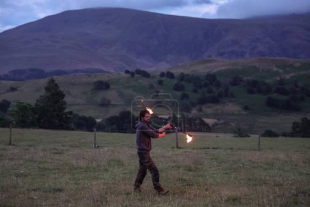 Téléchargez les photos : Un participant fait tournoyer un bâton de feu pendant qu'ils divertissent les spectateurs pendant la célébration du solstice d'été du Cercle de pierre de Castlerigg, Royaume-Uni, 20 juin 2023 - en image libre de droit