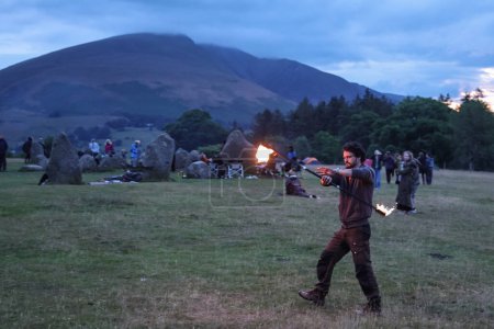 Téléchargez les photos : Un participant fait tournoyer un bâton de feu pendant qu'ils divertissent les spectateurs pendant la célébration du solstice d'été du Cercle de pierre de Castlerigg, Royaume-Uni, 20 juin 2023 - en image libre de droit