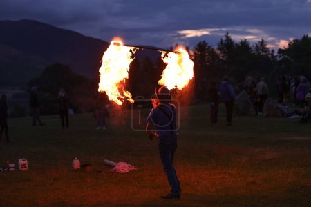 Foto de Un asistente hace girar un palo de fuego mientras entretienen a los espectadores durante la celebración del solsticio de verano del Círculo de Piedra de Castlerigg, Reino Unido, 20 de junio de 2023 - Imagen libre de derechos