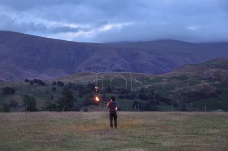 Téléchargez les photos : Un participant fait tournoyer un bâton de feu pendant qu'il divertit les spectateurs pendant le Cercle de pierre de Castlerigg. Célébration du solstice d'été, Royaume-Uni, 20 juin 2023 - en image libre de droit