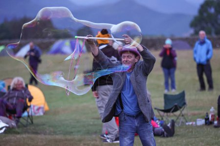 Téléchargez les photos : Un participant divertit alors qu'il souffle des bulles géantes pendant le Cercle de pierre de Castlerigg. Célébration du solstice d'été, Royaume-Uni, 20 juin 2023 - en image libre de droit