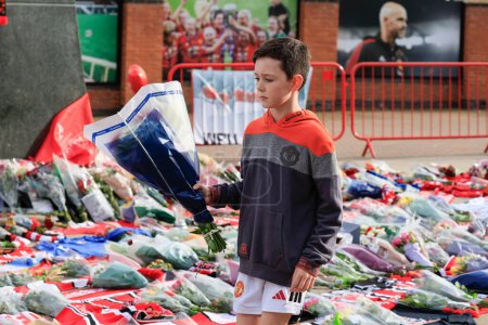 Téléchargez les photos : Un jeune fan de United laisse quelques fleurs en hommage au regretté Sir Bobby Charlton devant Old Trafford, Manchester, Royaume-Uni, 23 octobre 2023 - en image libre de droit