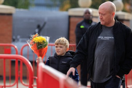 Téléchargez les photos : Un jeune fan apporte quelques fleurs en hommage au regretté Sir Bobby Charlton devant Old Trafford, Manchester, Royaume-Uni, 23 octobre 2023 - en image libre de droit