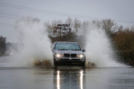 Foto de Un coche hace su camino a través de la carretera inundada causada por tormentas y fuertes lluvias en la A656 cerca de Leeds en Barnsdale Road A656, Allerton Bywater, Castleford, Reino Unido, 2 de enero de 2023 - Imagen libre de derechos
