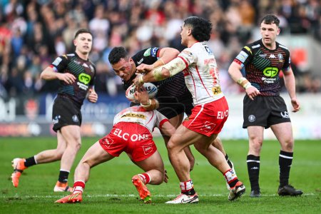Photo for Tyler Dupree of Wigan Warriors is tackled by Matt Whitley of St. Helens and Sione Matautia of St. Helens during the Betfred Super League Round 6 match St Helens vs Wigan Warriors at Totally Wicked Stadium, St Helens, United Kingdom, 29th March 2024 - Royalty Free Image