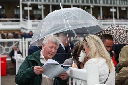 Foto de Racergoers se cubre cuando comienza a llover durante el Randox Grand National 2024 Opening Day en Aintree Racecourse, Liverpool, Reino Unido, 11 de abril 202 - Imagen libre de derechos