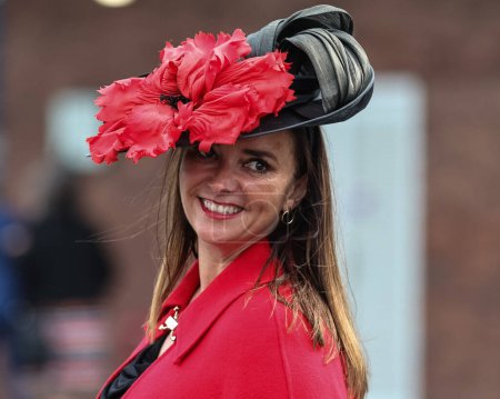 Foto de Un corredor de carreras con un vestido rojo y un sombrero negro con una gran flor roja llega durante el Gran Día Nacional de Randox 2024 en el hipódromo Aintree, Liverpool, Reino Unido, 13 de abril 202 - Imagen libre de derechos