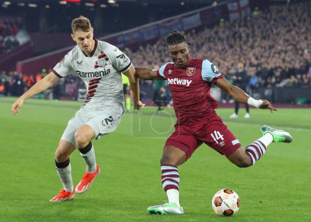Photo for Mohammed Kudus of West Ham United crosses the ball while under pressure from Josip Stanii of Bayer Leverkusen, during the UEFA Europa League Quarter-Final match West Ham United vs Bayer 04 Leverkusen at London Stadium, London, United Kingdom - Royalty Free Image