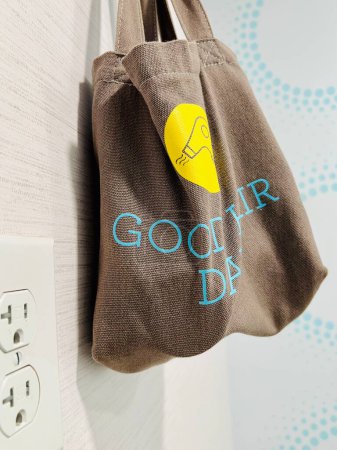 Photo for Interior of motel room bathroom brown cloth bag with cheerful good day slogan, holding a small hair dryer - Royalty Free Image