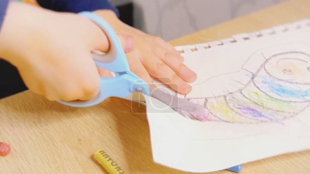 a child learns to use scissors, a preschool boy holds scissors in his hand and cuts out an image of a rainbow goose from paper. Development, fine motor skills, the child receives home education
