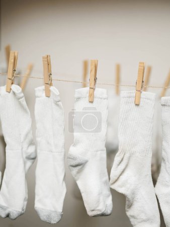 Weiße Socken, die an Seilen befestigt sind, um in Innenräumen an der Luft zu trocknen, um Energiekosten zu sparen. Vertikales Bild