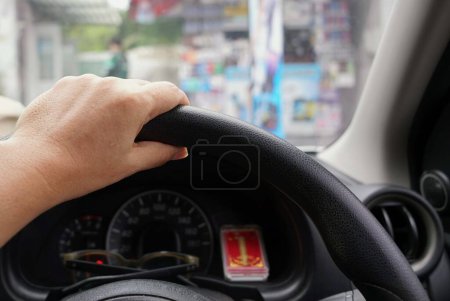A hand on the steering wheel of a car with blurred background, travel concept.
