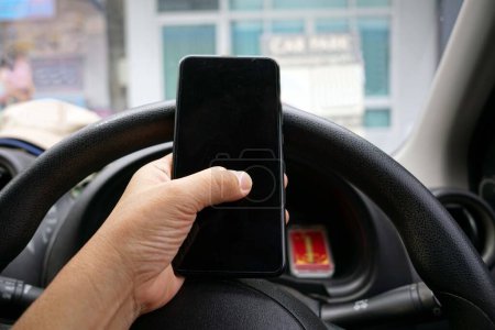 Téléchargez les photos : Gros plan d'une main tenant un smartphone au volant d'une voiture, concepts d'avertissement. - en image libre de droit