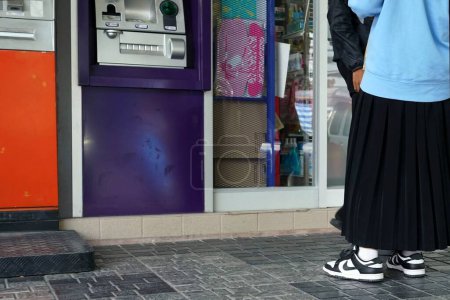 Foto de Una mujer parada frente a un cajero automático esperando a retirarse con amigos - Imagen libre de derechos