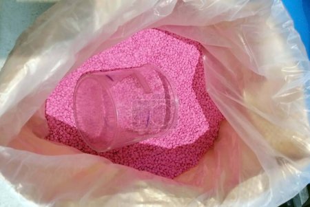 Un frasco de vidrio en una bolsa de pellets de plástico rosa para producir un disco fonógrafo. 