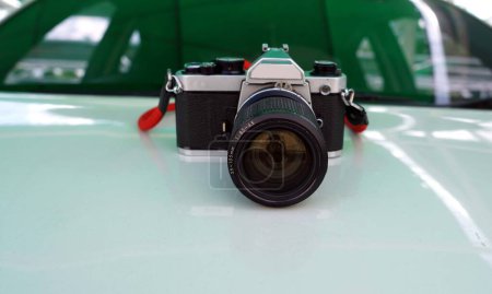 Photo for A retro film camera with red strap isolated on a front body car backside a car glass. - Royalty Free Image
