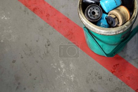 Téléchargez les photos : Beaucoup d'un vieux filtre à huile dans la poubelle sur fond de sol en béton avec ligne rouge dans un atelier de réparation automobile. - en image libre de droit