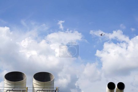 Foto de Chimeneas industriales contra como el avión vuela volando en el cielo azul con nubes blancas, fondo industrial, conceptos de medio ambiente. - Imagen libre de derechos