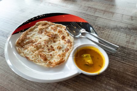 Photo for Close-up of simple no frills roti canai with dhal curry served in plate on wooden table - Royalty Free Image