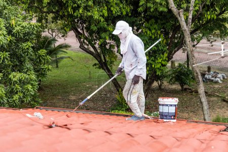 Trabajador pintura techo rojo con rodillo en el edificio residencial después de aplicar capa de cimentación druing renovación