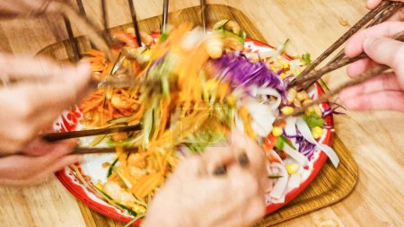 Photo for People mixing and tossing yusheng or yee sang in Japanese recipe with salmon sashimi during Chinese New Year dinner celebration, believed to bring luck. Slow shutter speed with motion blur intended. - Royalty Free Image