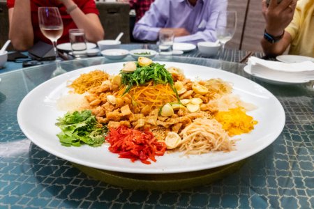 Photo for Serving of auspicious yusheng or yee sang with abalone in restaurant during Chinese New Year celebration in Malaysia with diners seated - Royalty Free Image