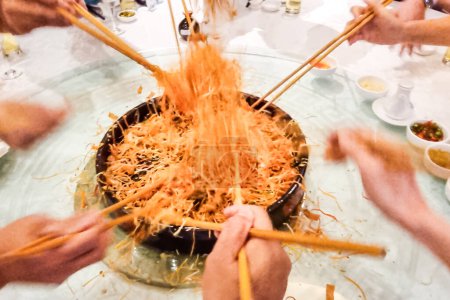 People mixing and tossing yusheng or yee sang during Chinese New Year dinner celebration, believed to bring luck. Slow shutter speed with motion blur intended.