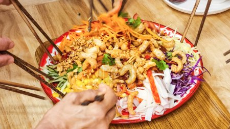 Photo for People mixing and tossing yusheng or yee sang with raw salmon sashimi during Chinese New Year dinner celebration, believed to bring luck - Royalty Free Image