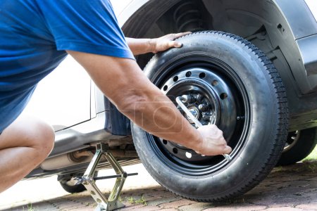 Photo for Person attempting to tighten nuts onto temporary wheel after replacing the ruptured flat tire on the street - Royalty Free Image