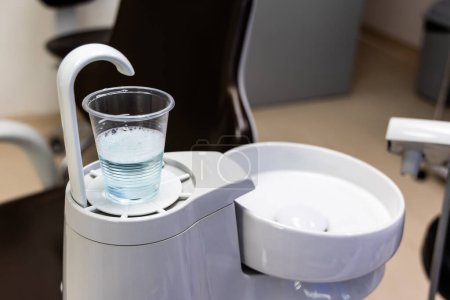 Disposable glass filled with CHX mouth rinse solution next to spiotoon bowl in dental clinic