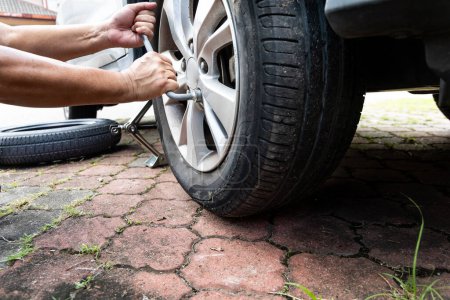 Photo for Person using wrench tool to remove punctured ruptured flat tire from automobile at road side - Royalty Free Image