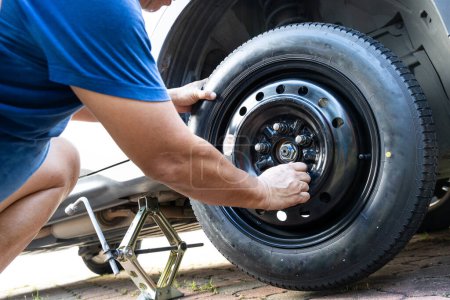 Photo for Person attempting to tighten nuts onto temporary wheel after replacing the ruptured flat tire on the street - Royalty Free Image