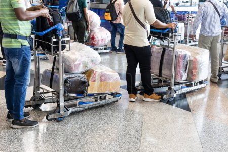 Téléchargez les photos : Voyageurs à l'aéroport avec des bagages sur un chariot enveloppé d'un film protecteur pour la sécurité - en image libre de droit