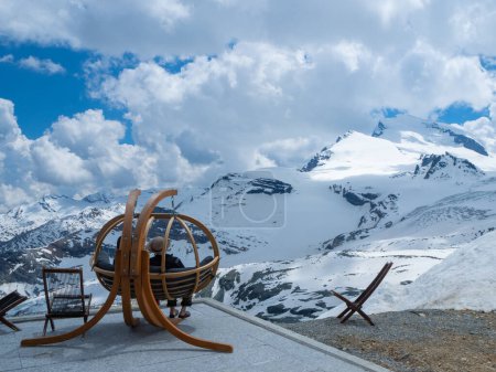 Photo for Enjoying the alpine panorama in a comfortable hanging seat on the terrace of Britanniahuette, Switzerland. View of Strahlhorn peak and Allalin glacier. - Royalty Free Image