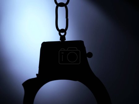 Handcuffs sillhouette agains blue light background close up shot selective focus