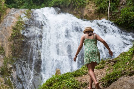 Tourist woman walks towards a waterfall, in the Peruvian jungle.