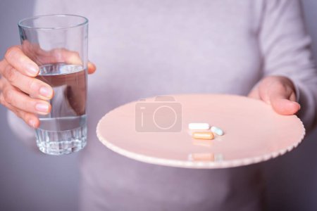 Unrecognizable person with a plate of pills and a glass of water.