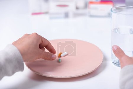 Hands of person about to be medicated with pills on a plate and a glass of water.