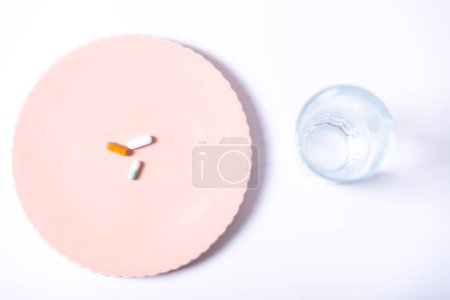 Top view of tablets on a plate next to a glass of water, on a white background.