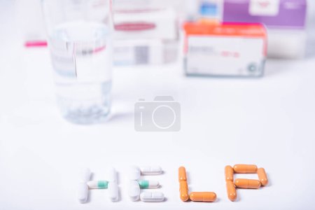 Word HELP made with medical pills and in the background several boxes of medicines.