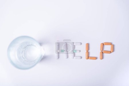 Word HELP made with medical pills on the side of a glass of water.