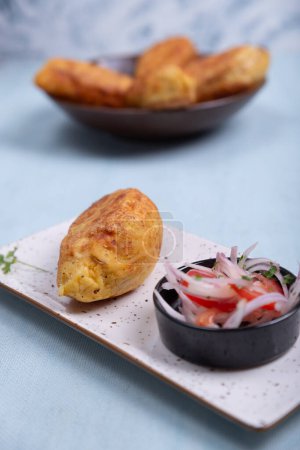 Delicious Peruvian comfort food: potato stuffed with meat, accompanied by an onion and tomato salad.