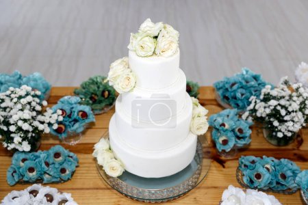 gâteau d'anniversaire blanc avec quatre parties, avec des fleurs blanches et divers bonbons sur la table