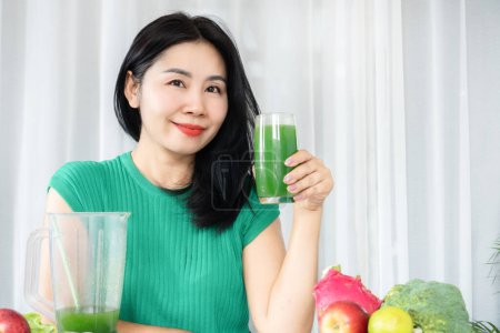 Photo for Nourishing Asian woman embracing health with a glass of green fruit and vegetable juice rich in natural fiber - Royalty Free Image