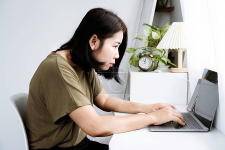 Konzept der asiatischen Frau mit Kyphose: Seitenansicht des Laptops Arbeit mit gekrümmtem Rücken, vorderer Kopfhaltung und Wirbelsäulenverkrümmung