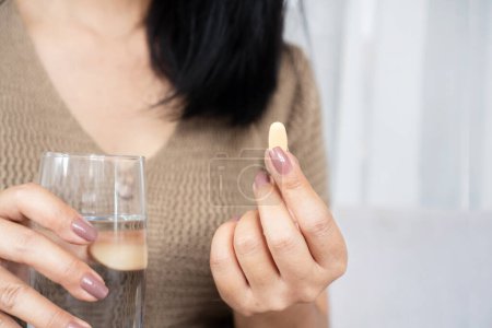 Téléchargez les photos : Gros plan de la main d'une femme prenant un supplément de vitamine C avec un verre d'eau - en image libre de droit